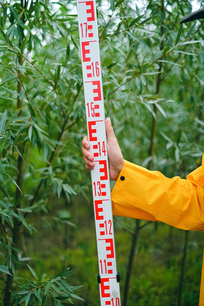 A farmer measuring plant growth with a ruler in a lush farmland setting.