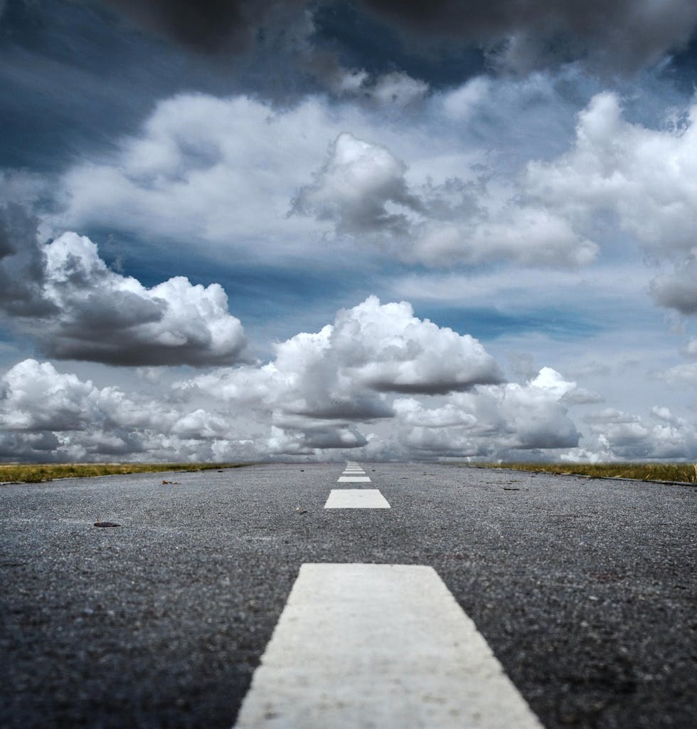 A straight road stretched toward a dramatic sky filled with fluffy clouds, creating a sense of journey.